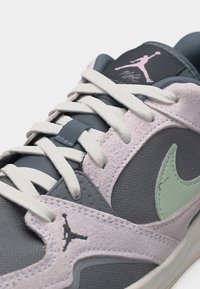Κοντινό πλάνο ενός γκρι και ανοιχτό ροζ αθλητικού παπουτσιού Jordan με λευκά κορδόνια, που δείχνει το λογότυπο Jumpman και το λογότυπο Nike σε μέντα πράσινο χρώμα.