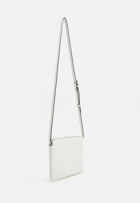 Sac en cuir blanc en bandoulière avec une forme rectangulaire plate et une bandoulière réglable. Présente un contour noir contrastant le long des bords.