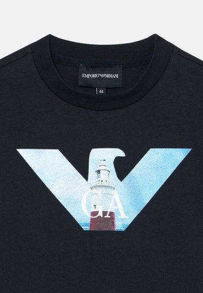 Schwarzes Baumwoll-T-Shirt mit einem großen blau-weißen Grafikdesign, das einen Leuchtturm innerhalb eines stilisierten "EA"-Logos zeigt. Runder Ausschnitt mit Nähten.