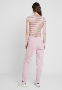 Světle růžové bavlněné džíny se zúženým střihem a dvěma zadními kapsami, v kombinaci s těsně padnoucím tričkem s multikolorovými pruhy. Bílé tenisky dotvářejí celkový vzhled.