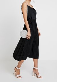 Czarna plisowana spódnica midi połączona z czarną satynową koszulą na ramiączkach oraz różowymi sandałami na słupku, uzupełniona okrągłą torebką z koralików.