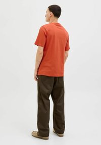 Terracotta kortærmet t-shirt med rund halsudskæring, parret med løstsiddende mørkegrønne bukser og beige slip-on sko.
