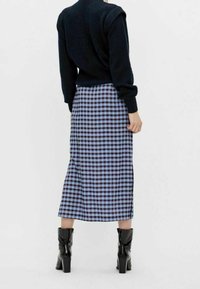 Black sweater, long blue and black checked skirt, side slit, paired with knee-high black heeled boots, viewed from the back.