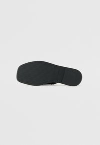 Black shoe sole featuring a textured pattern, rounded shape, with a smooth edge and a firm construction. Notable branding visible.