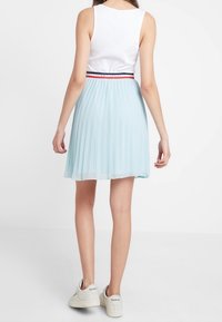 Lichtblauwe geplooide rok met een zwart, rood en witte tailleband; gecombineerd met een witte ribbel tanktop en grijze sneakers.