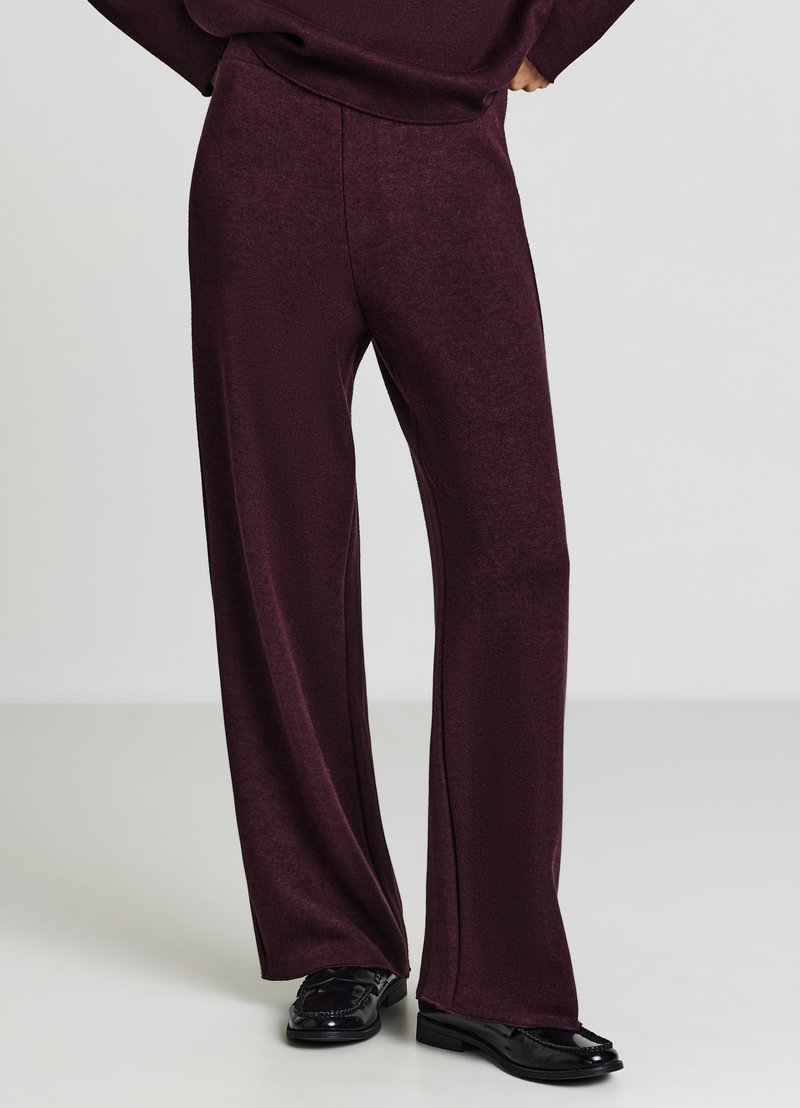 Weit geschnittene, burgunderrote Hose aus einem weichen, strukturierten Stoff mit hoher Taille und glattem Finish. Kombiniert mit schwarzen Loafers.