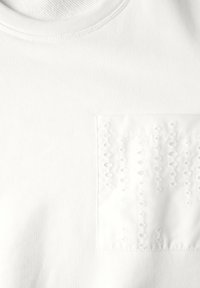 T-shirt blanc en coton avec un patch texturé présentant une broderie en relief dans un motif vertical sur la zone du côté gauche de la poitrine.