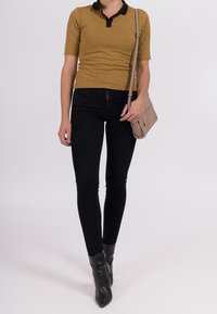 Top corto a maniche corte a coste color senape con colletto nero, abbinato a jeans skinny neri e stivaletti con punta. Borsa a tracolla beige con dettaglio a zip.