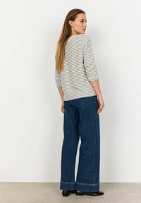 Stripet grå og hvid langærmet top parret med brede mørke denimbukser. Bukserne har en rå kant, og toppen har opkrøllede ærmer.