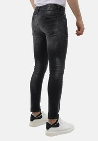 Zwarte slim-fit jeans met een vervaagd uiterlijk, voorzien van een vijf-pocket ontwerp en subtiele slijtage, gecombineerd met witte sneakers.