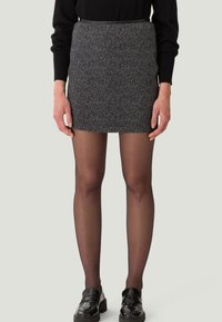 Jupe mini noire à motif avec un design ajusté, en tissu texturé, dotée d'une taille fine, associée à des collants noirs transparents et des chaussures noires épaisses.