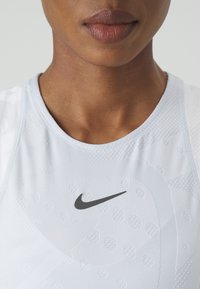 Fehér sportfelső helyi mintázattal és szürke Nike swoosh logóval a mellkason. Kerek nyakkivágású és testhezálló fazonú.