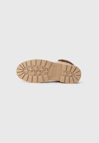 Botte en daim marron avec une semelle en caoutchouc texturée beige, présentant des crampons profonds et un motif de croix, offrant adhérence et traction.