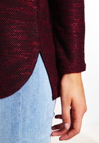 Burgundy texturerad tröja med sidoflikar, kombinerad med ljusblå denim. Har en lös passform och långa ärmar som framhäver tygets detaljer.