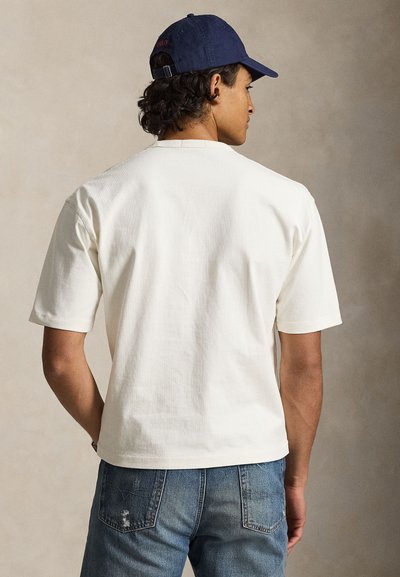 Λευκό βαμβακερό T-shirt με κοντά μανίκια και στρογγυλή λαιμόκοψη, συνδυασμένο με ξεβαμμένα μπλε τζιν. Απλός, λιτός σχεδιασμός.