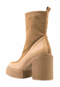 Botín de mujer en tono marrón claro con tacón cuadrado, parte superior de ante, detalles en cuero liso y una lengüeta en la parte trasera.