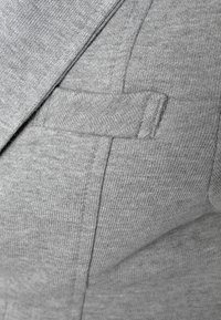 Grått tyg med en texturerad stickning och en slät, platt fickdetalj på sidan, som visar upp en modern skräddarsydd design.