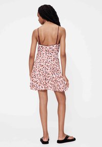 Lillelise mustriga lühike kleit õhukeste õlapaeltega, millel on mitmevärviline abstraktne mustriline heleroosa taust, valmistatud pehmest kangast.