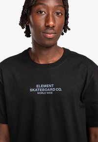 Black cotton t-shirt featuring "ELEMENT SKATEBOARD CO. WORLD WIDE" in light blue lettering, with a classic crew neck design.