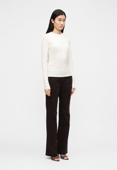 Μακρυμάνικο κρεμ ριμπ τοπ συνδυασμένο με σκούρο καφέ παντελόνι φαρδιάς γραμμής. Το τοπ έχει κάθετες ρίγες και στρογγυλή λαιμόκοψη.