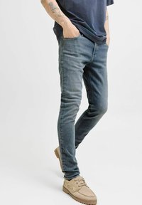 Tunna blå denimjeans med blekta detaljer, två framfickor och midjehöjd, kombinerade med beige snörskor.