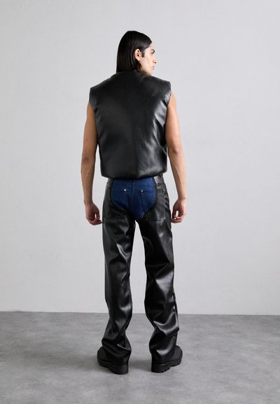 Black leather sleeveless top and shiny black leather pants, featuring blue denim accents on the back, worn with thick-soled black shoes.