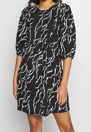 Musta mekko, jossa on abstrakteja valkoisia ja vaaleanpunaisia aalto-kuvioita. Varustettu pullistetuilla hihoilla ja kerätyllä vyötäröllä, valmistettu pehmeästä, laskeutuvasta kankaasta.