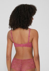 Różowa koronkowa biustonosz z regulowanymi ramiączkami, teksturowanym kwiatowym wzorem i zapięciem na haczyk z tyłu. W zestawie z pasującymi różowymi koronkowymi figami.