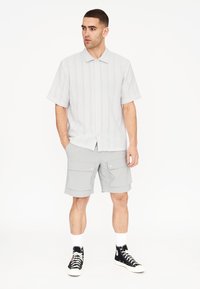 Camisa de botones de manga corta de color gris claro con Rayas verticales, combinada con pantalones cortos grises tipo cargo y zapatillas altas negras.