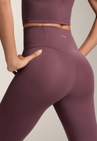 Legíny s vysokým pásom v hlbokom mave odtieni, vyrobené z hladkej, elastickej tkaniny s elegantným strihom a detailmi švov.