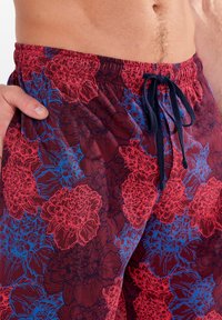 Lätta simshorts med ett blommönster i röd och blått på en mörk bakgrund. Elastisk midja med en marinblå dragsko.