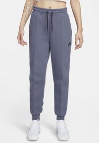 Nike joggingbroeken in een gedempte paarse kleur, gemaakt van zacht materiaal. Ze hebben een elastische tailleband met koord en zijzakken. Zwart logo op de linker dij.