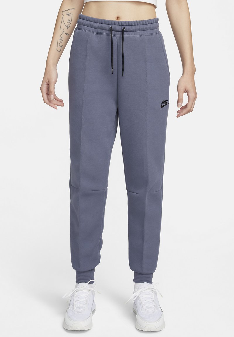 Nike joggingbroeken in een gedempte paarse kleur, gemaakt van zacht materiaal. Ze hebben een elastische tailleband met koord en zijzakken. Zwart logo op de linker dij.
