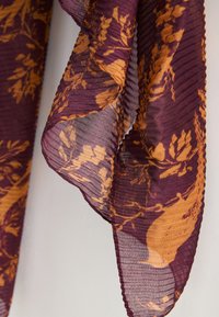 Écharpe à motifs violets et orange avec une texture plissée, présentant des motifs botaniques et un tissu léger et transparent.