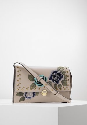Beige leren crossbodytas met bloemenborduurwerk, gouden studs en een gouden sluiting, tentoongesteld op een wit voetstuk tegen een effen achtergrond.