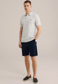 Világosszürke pólóing rövid ujjakkal, tengerészkék sort és sötét slip-on cipő. Kis logó található a mellkason. Egyszerű dizájn.