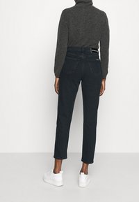 Dark denim jeans with a high waist and straight leg fit, paired with a gray turtleneck and white sneakers. Minimalistic design, classic stitching.