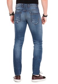 Blauwe denim jeans met een slim fit, voorzien van vervaging, versleten details, twee achterzakken en een standaard tailleband. Gedragen met casual schoenen.