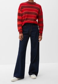 Gestreifter Pullover in Rot und Braun mit Rundhalsausschnitt, kombiniert mit dunkelblauen weit geschnittenen Jeans und weißen Sneakern.