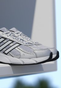 Športové topánky v šedobielom farebnom prevedení, sieťovinový zvršok, tri čierne pruhy, textúrovaná podrážka a výrazná špička.