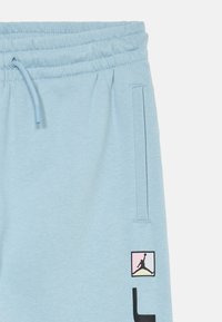 Svetlomodré teplákové nohavice s elastickým pásom, šnúrkou a bočnou kapsou, s malým farebným logom Jumpman blízko kapsy.