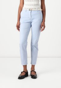 Světle modré slim-fit chinos s hladkým povrchem a poutky na pásek, v kombinaci s černými lakovými Mary Jane botami.