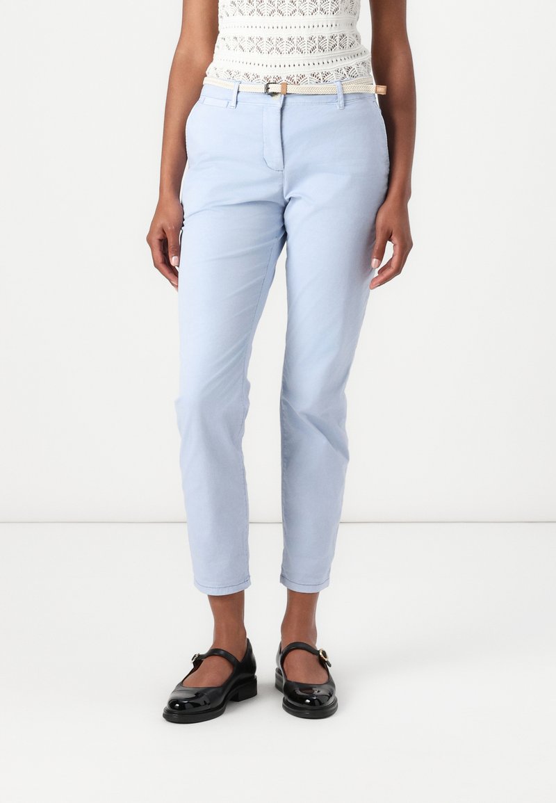 Světle modré slim-fit chinos s hladkým povrchem a poutky na pásek, v kombinaci s černými lakovými Mary Jane botami.