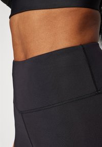 Black high-waisted leggings with smooth texture and contrasting stitching details. Stretchy fabric designed for comfort and flexibility.