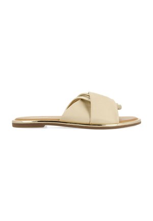 Sandale plate beige avec des lanières croisées, dessus en synthétique lisse, bout arrondi, semelle plate et bord métallique doré.