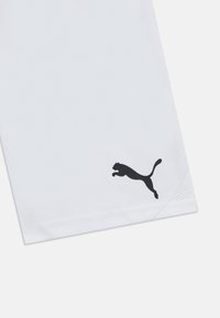 Shorts de sport blancs avec un logo noir, présentant une texture lisse, une coupe droite et des détails en mesh au bas de l'ourlet.