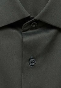 Tessuto di camicia verde scuro con una superficie liscia, caratterizzato da un colletto a punta e un bottone nero al collo. Dettagli di cucitura sottili visibili.