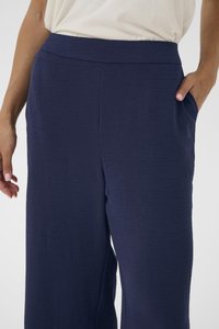 Pantalon large bleu marine en tissu texturé avec une taille plate et des poches latérales, offrant une coupe décontractée et un design minimaliste.