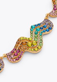 Collana in tono oro con un design ondulato decorato con strass multicolori in rosa, verde, blu e viola. Texture liscia.