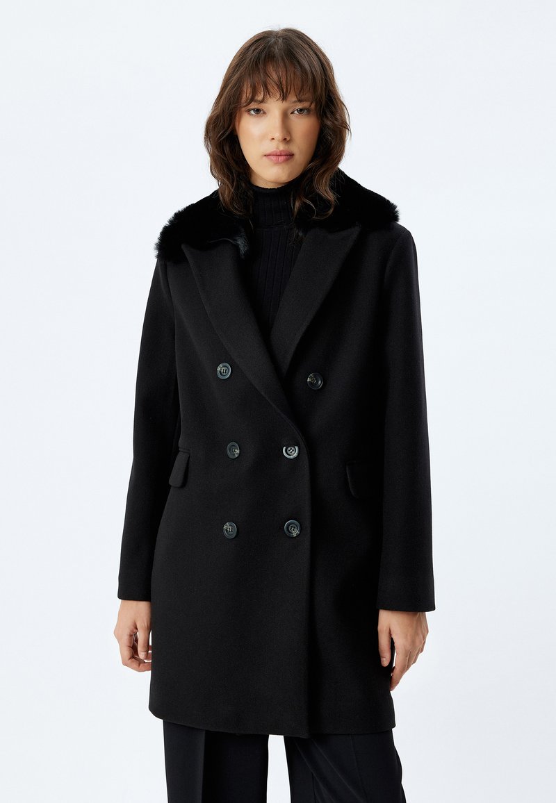 Cappotto di lana nero con design doppiopetto, colletto in pelliccia sintetica e due tasche frontali. Dotato di grandi bottoni neri e spalle strutturate.
